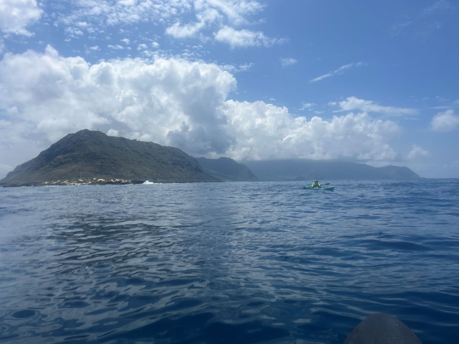 A single kayaker with Kaena Point and the Waianae mountains in the background