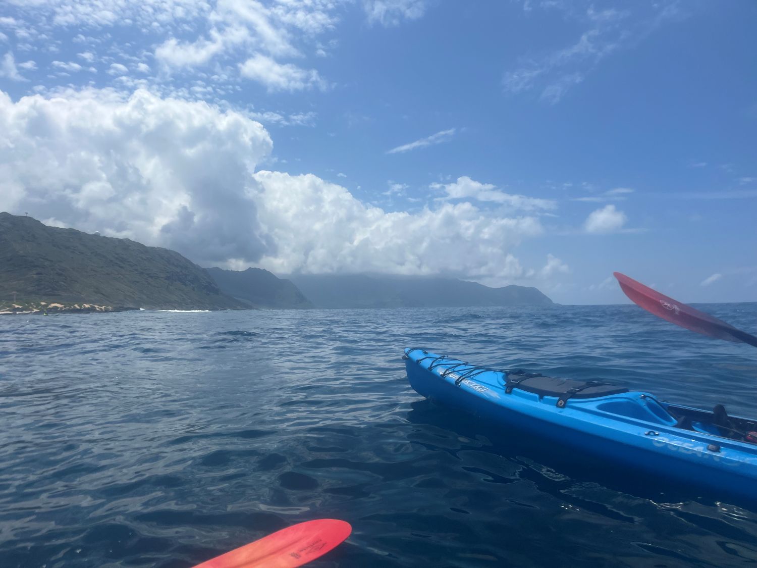 The bow of a kayak with the Waianae side of Kaena Point in the background