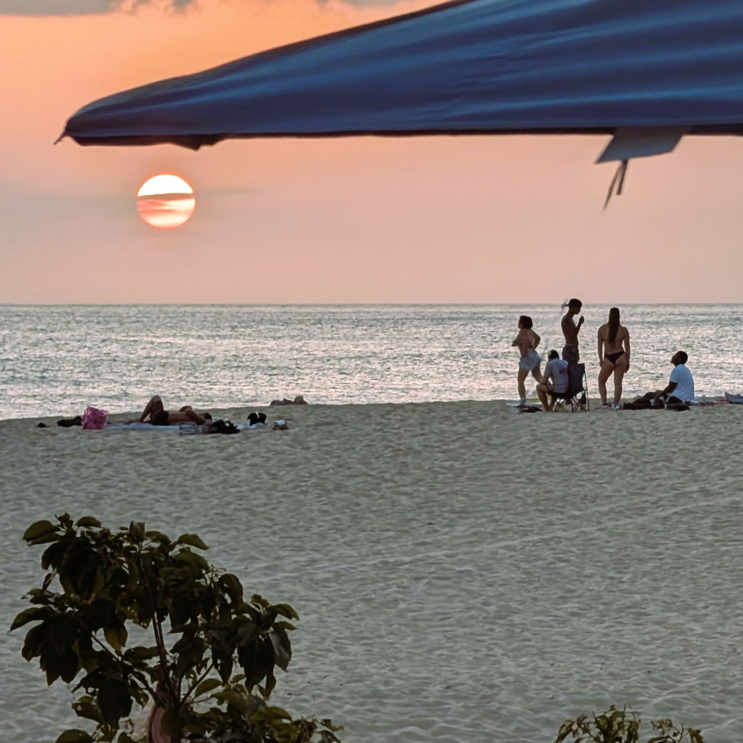Setting sun under a canopy eave with silhouetted people on the beach