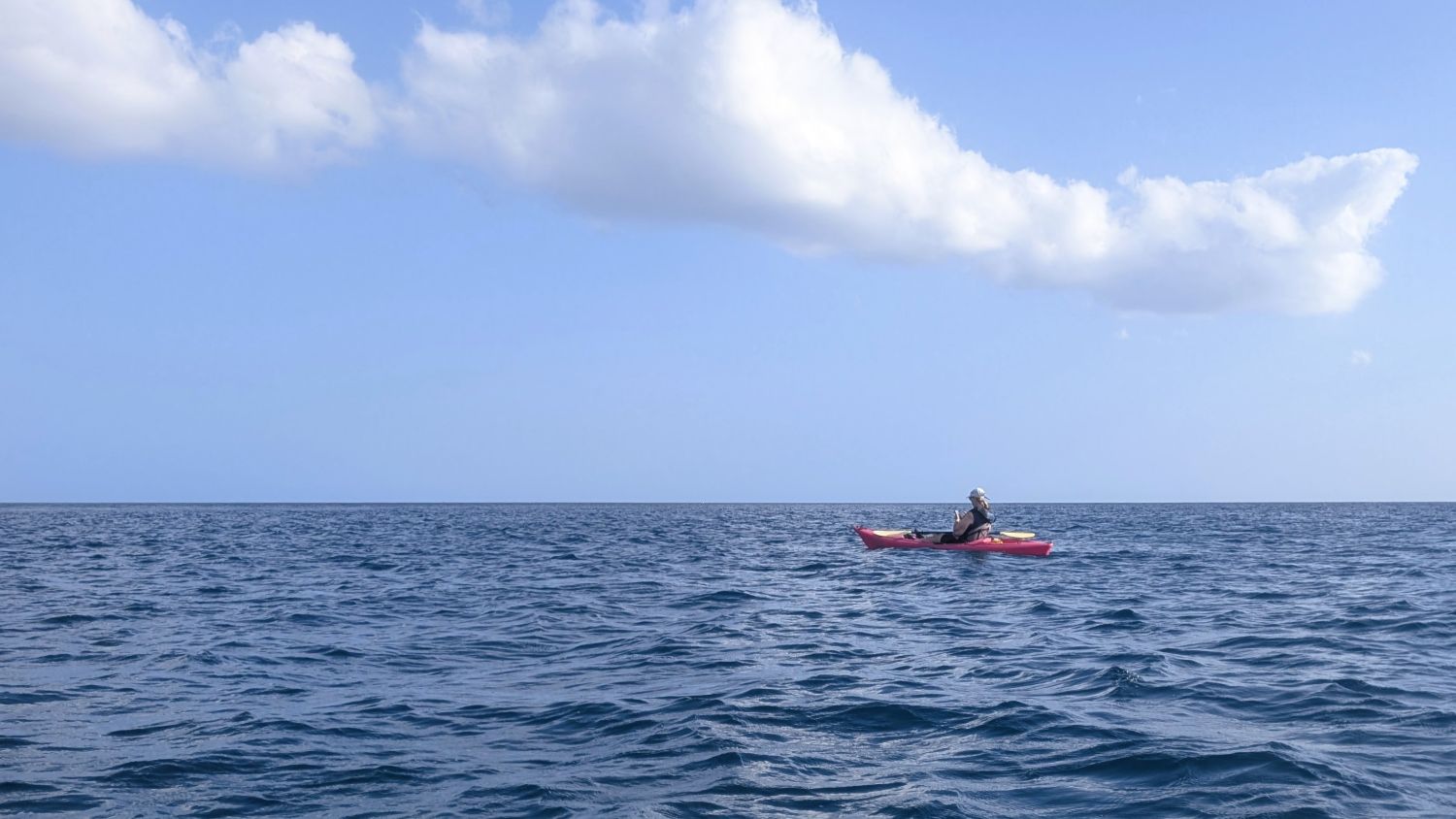 Lone kayaker surrounded by ocean and blue sky