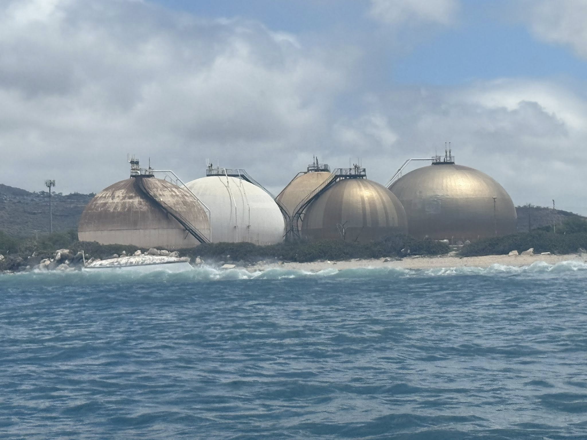 Grounded boat on shore with round storage tanks in background