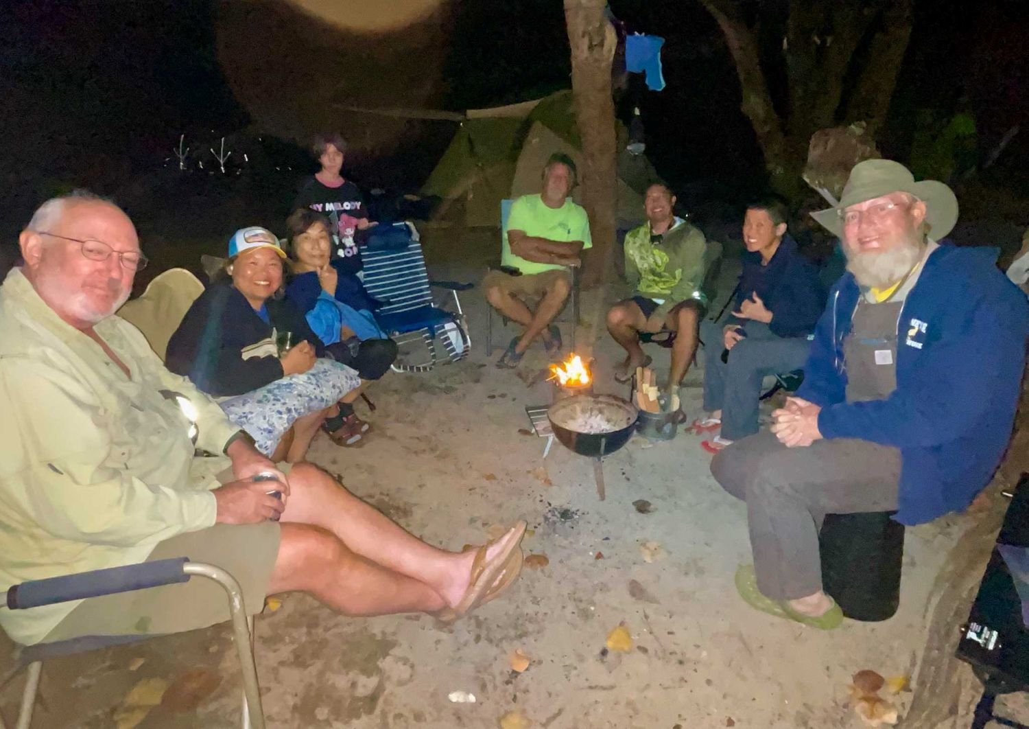 Eight people seated around a small campfire