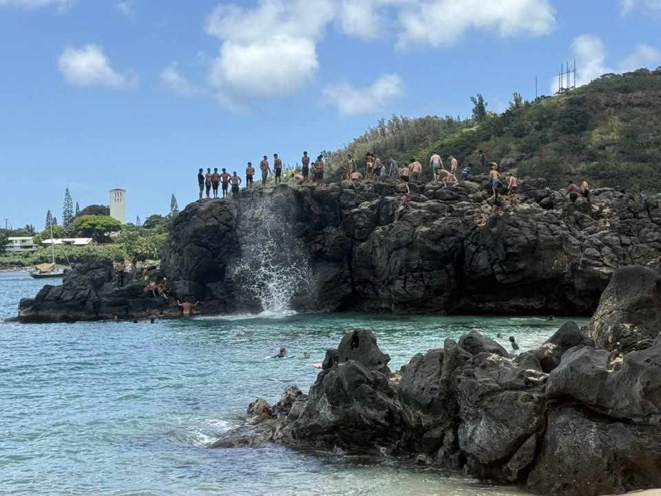 A big splash from a jumper off of the Waimea Bay jumping rock with lots of people on standing on the top of the rock