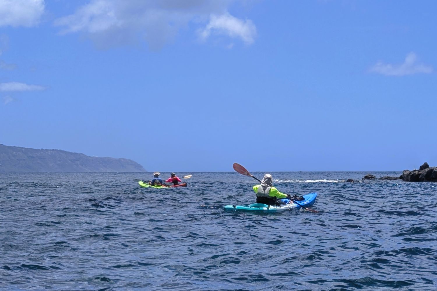Three kayakers paddling with Kaʻena Point on the horizon