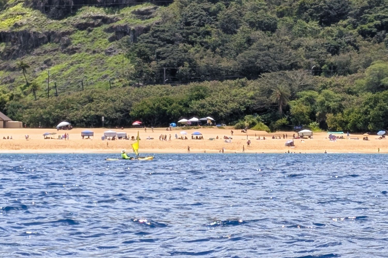 Kayaker with a yellow sail crossing in front of the Waimea Bay beach