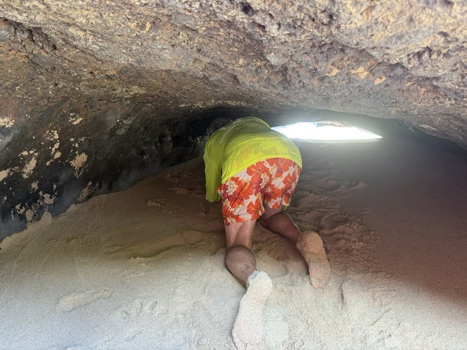 Man crawling into a sand filled cavern with a very low ceiling